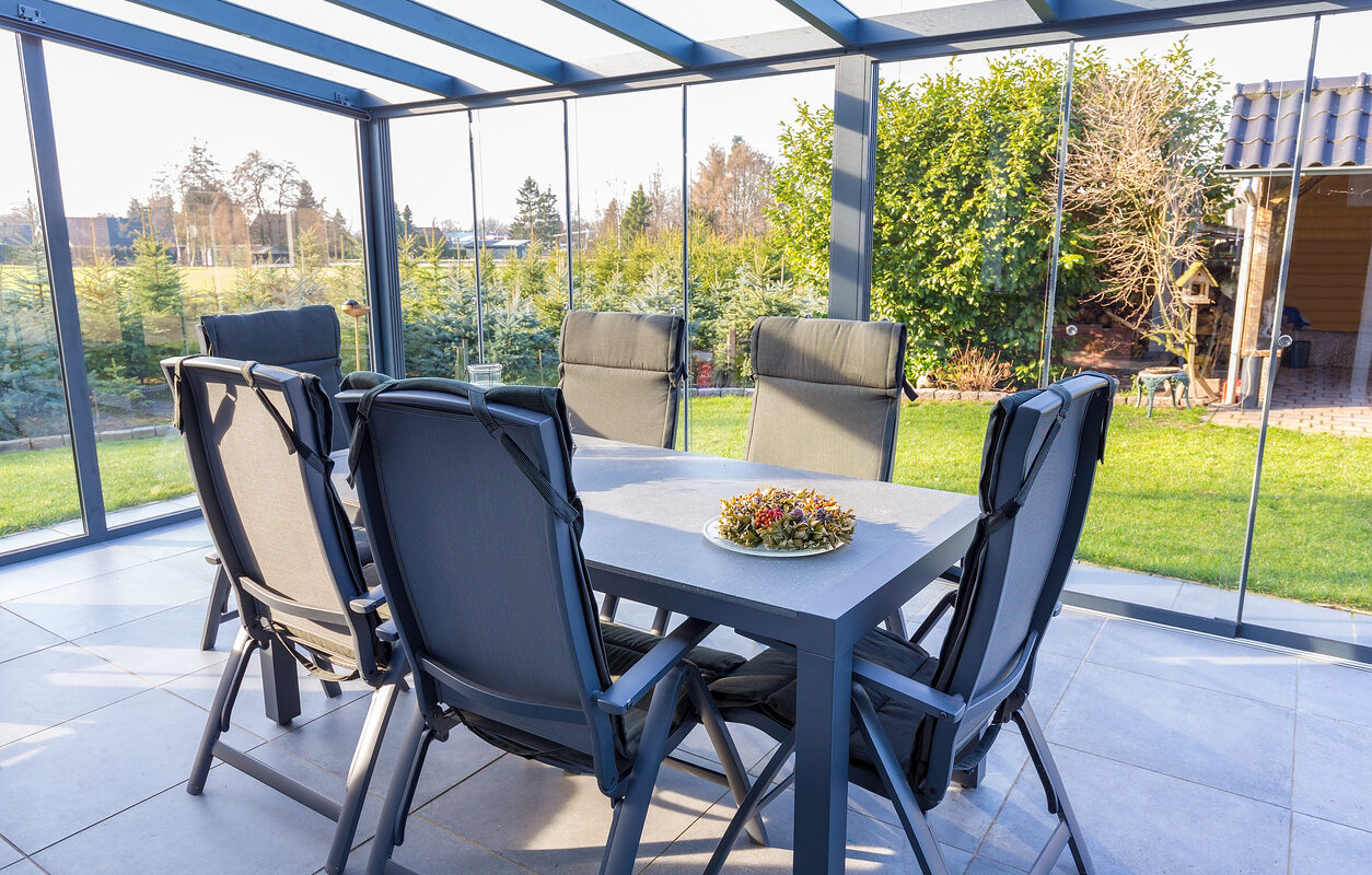 Conservatory of glass with table and chairs in garden. In this room you can enjoy sunny days even when the temperature outdoors is too low. It's as if you are outdoors in your garden.